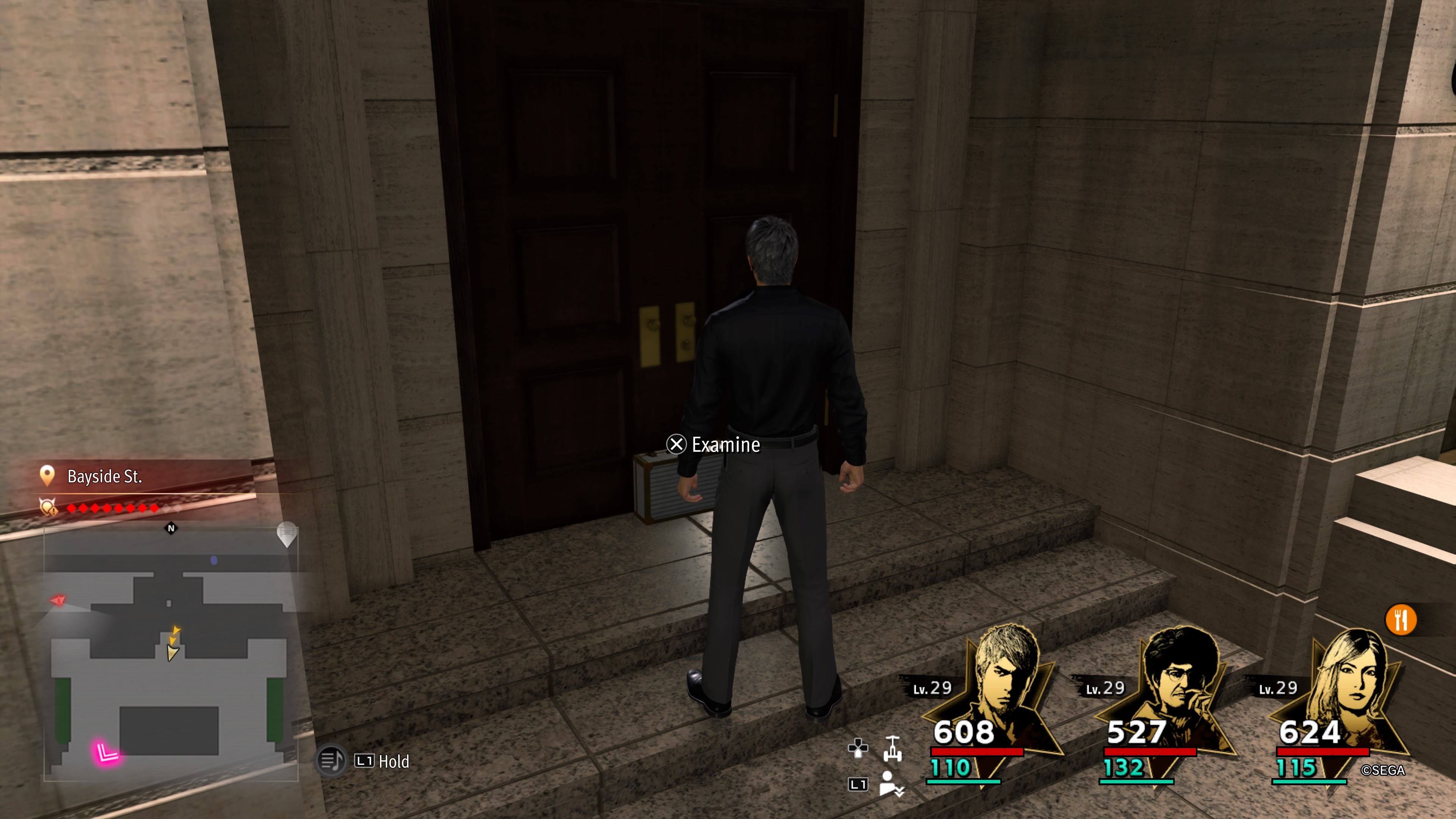 Kiryu parado frente a un gran edificio con un cofre del tesoro en las puertas de entrada en Like A Dragon: Infinite Wealth.