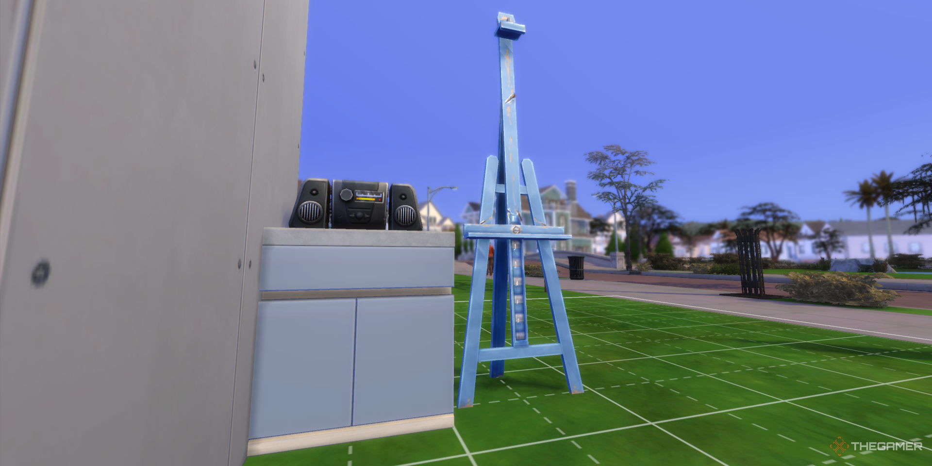 Un mostrador con una radio y un caballete azul se encuentran en el jardín delantero de un edificio sin terminar en Los Sims 4.