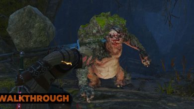 Geralt ducks under a rock thrown by an angry troll as they fight in the mouth of a cave by a lake.